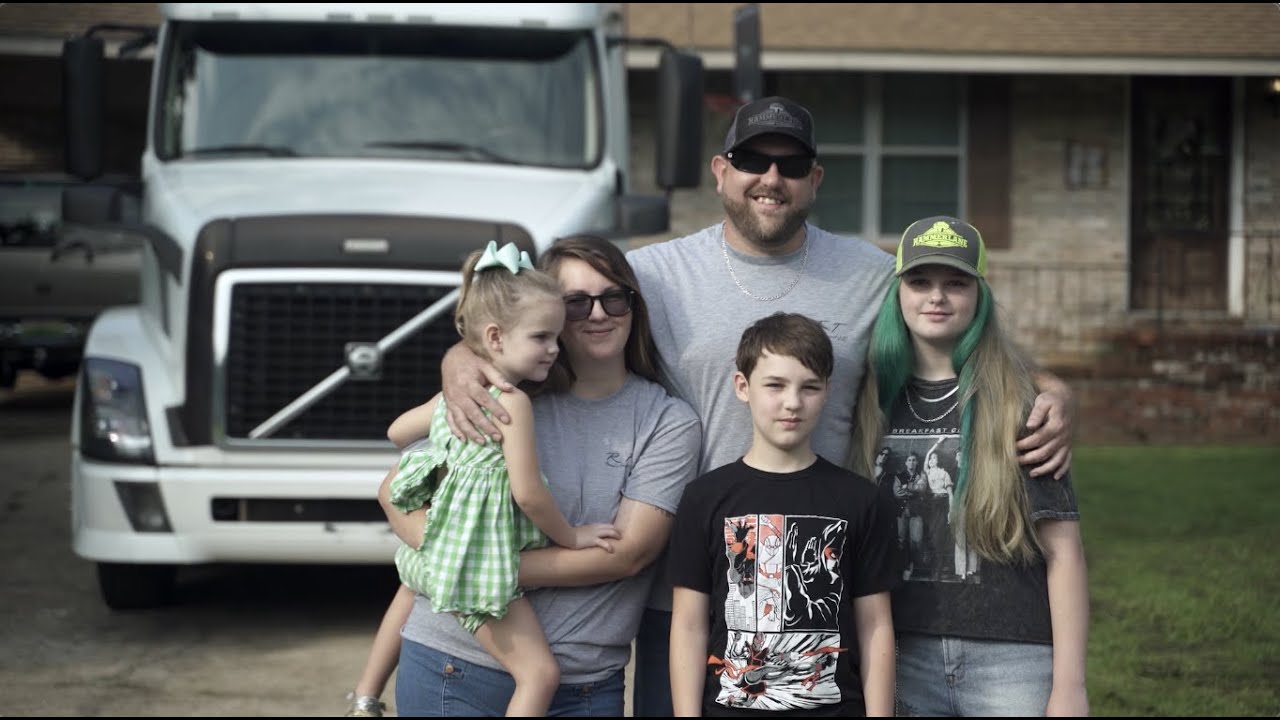 A truck driver greeting his family at home in front of his rig